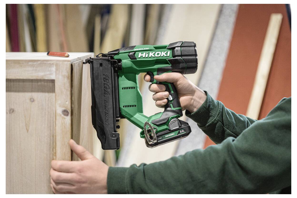 Person, der ein grünes tragbares HiKOKI-Nagelpistol verwendet, um Zierleisten an einem Holzschrank oder einer Holzplatte während der Schreinerei zu befestigen.