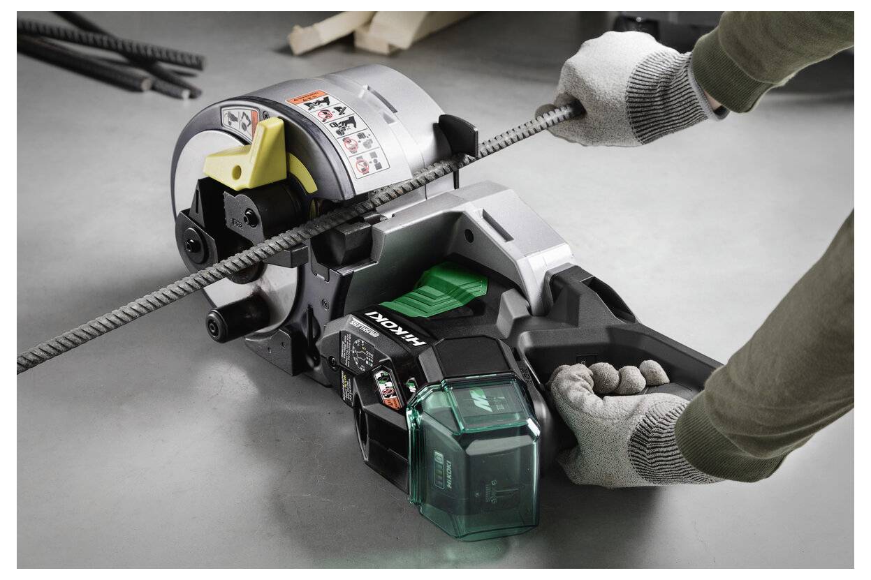 Handschuhe tragende Hände führen eine Metallbewehrung durch einen kabellosen Makita-Bewehrungsschneider auf einem Betonboden.