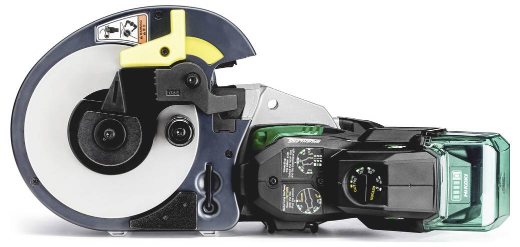 Hände in Arbeitshandschuhen führen eine Stahlstange in einen kompakten Makita-Arbeitstisch-Bewehrungsstabschneider/-bieger auf einem Werkstattboden ein.