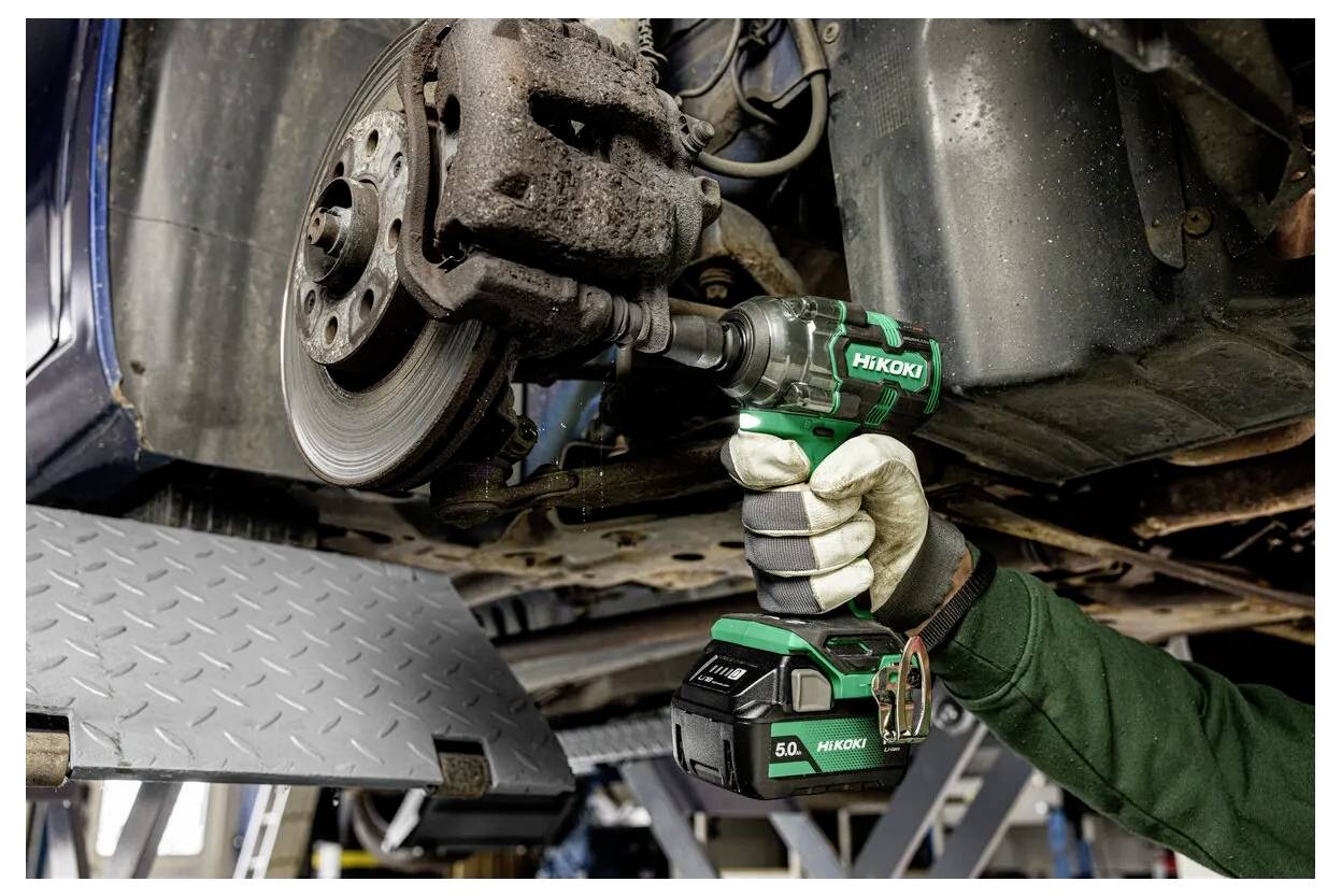 Ein Mechaniker verwendet einen kabellosen Schlagschrauber, um eine Radschraube eines Autos zu entfernen, während das Fahrzeug auf einer Serviceplattform angehoben ist.
