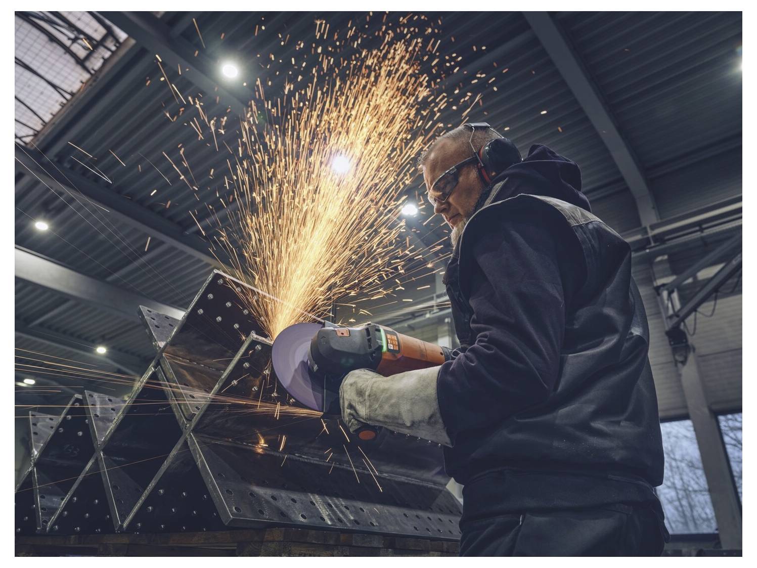 Arbeiter, der in einer Fabrik einen Winkelschleifera auf Metall verwendet, wobei Funken vom Schnittpunkt fliegen.