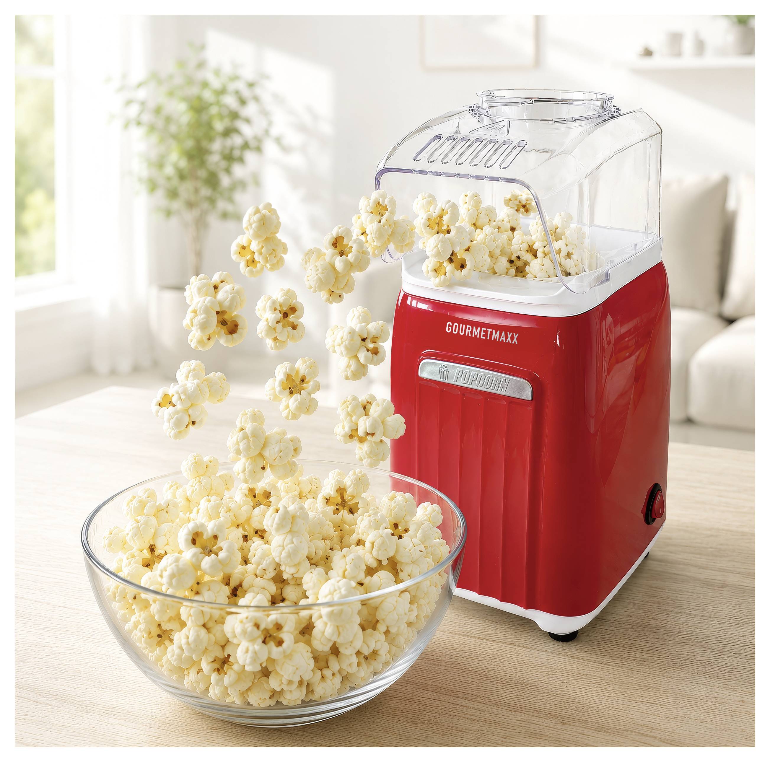 Ein roter Popcorn-Automat, der Popcorn in eine Glasschüssel auf einem Tisch in einem hellen Wohnzimmer verteilt.