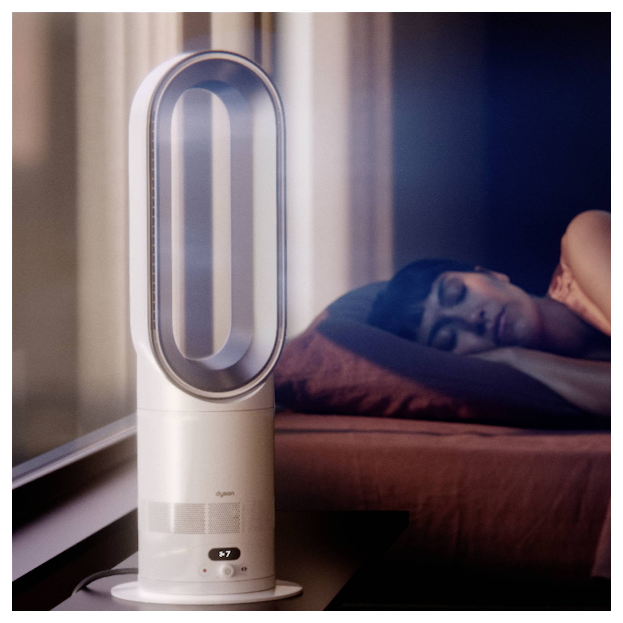 Ein blattloser Turmventilator oder eine Luftreinigungsanlage steht neben einer schlafenden Frau im Bett und deutet auf eine ruhige nächtliche Kühlungs- oder Luftreinigungsszene hin.