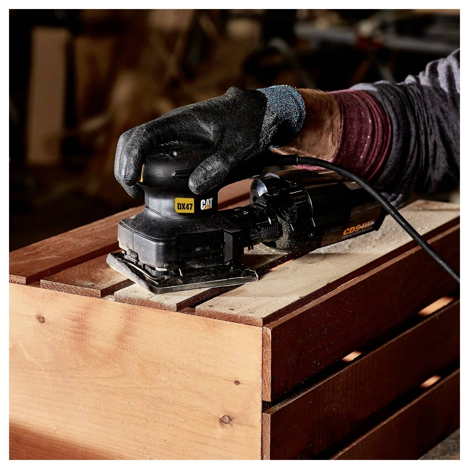 Handschuh-behandelte Hand, die ein Holzbrett mit einem schwarzen CAT-Elektroschleiffer auf einer Werkbank abschleifte.