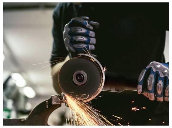 Person trägt Handschuhe und verwendet einen Winkelschleifer auf Metall, wobei Funken wegfliegen.