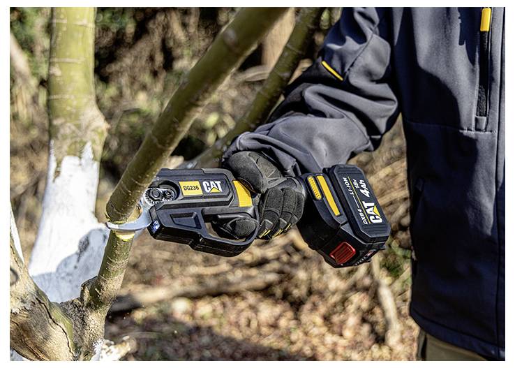 Eine Person benutzt eine schnurlose CAT-Astsäge, um einen Baumast im Freien zu schneiden, trägt Handschuhe und eine dunkle Jacke.