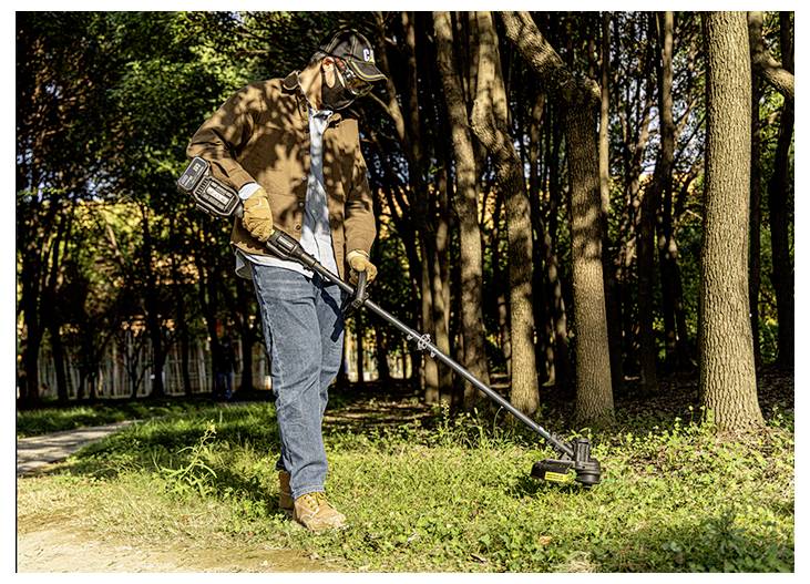 Eine Person, die einen Fadentrimmer verwendet, um Gras entlang eines bewaldeten Weges in einem Park zu schneiden.