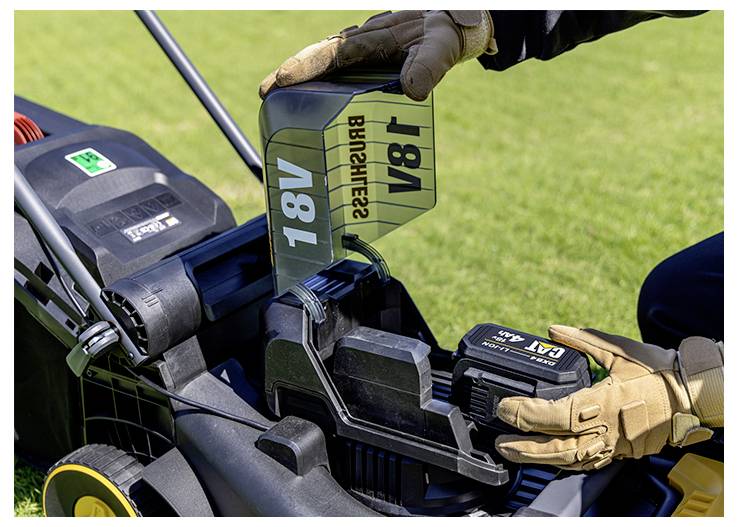 Handschuhe tragend werden eine 18V-Batterie in den Stromschlitz eines Rasenmähers im Freien auf Gras eingesetzt.
