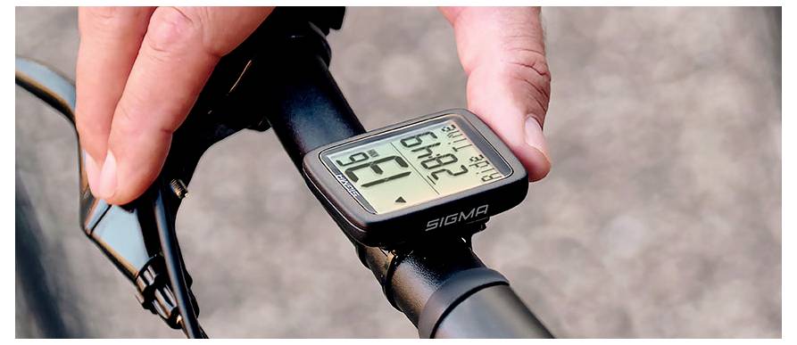 Nahaufnahme eines Fahrradlenkers mit einem digitalen Sigma-Fahrradcomputer, der Fahrtdaten anzeigt, während eine Hand diesen einstellt.