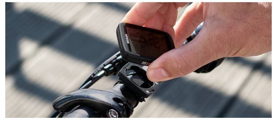 Nahaufnahme einer Hand eines Radfahrers, die einen am Lenker montierten Fahrradcomputer auf einem Fahrrad einstellt.