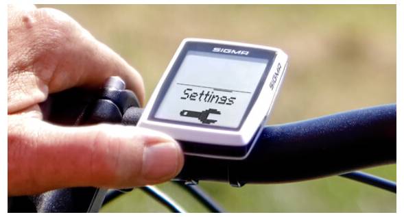 Eine Hand drückt eine Taste des Sigma Fahrradcomputers, während der Bildschirm 