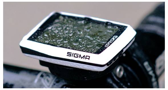 Nahaufnahme eines nassen Sigma-Fahrradcomputers, der auf dem Lenker montiert ist, mit Regentropfen auf dem Display.