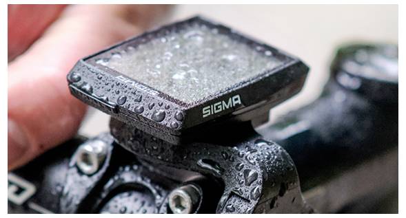 Nahaufnahme eines nassen Sigma-Fahrradcomputers, der auf einem Fahrradlenker montiert ist, mit Wassertropfen auf dem Gerät und dem Fahrradrahmen.