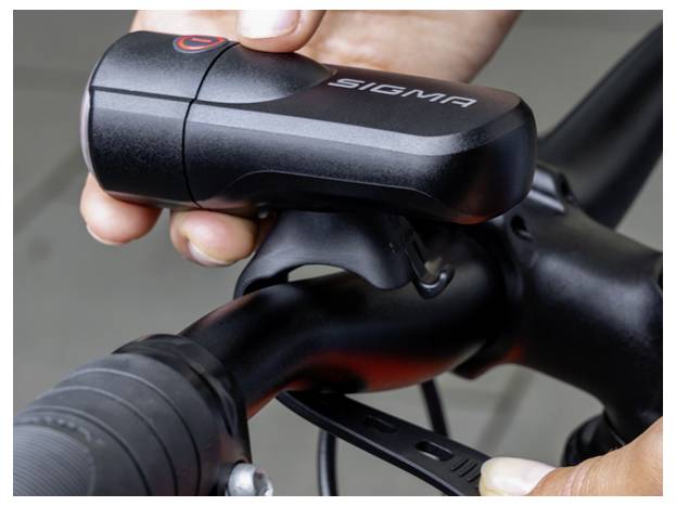 Nahaufnahme einer Sigma-Fahrradlampe, die an einem Fahrradlenker montiert wird, während Hände die Halterung festziehen.