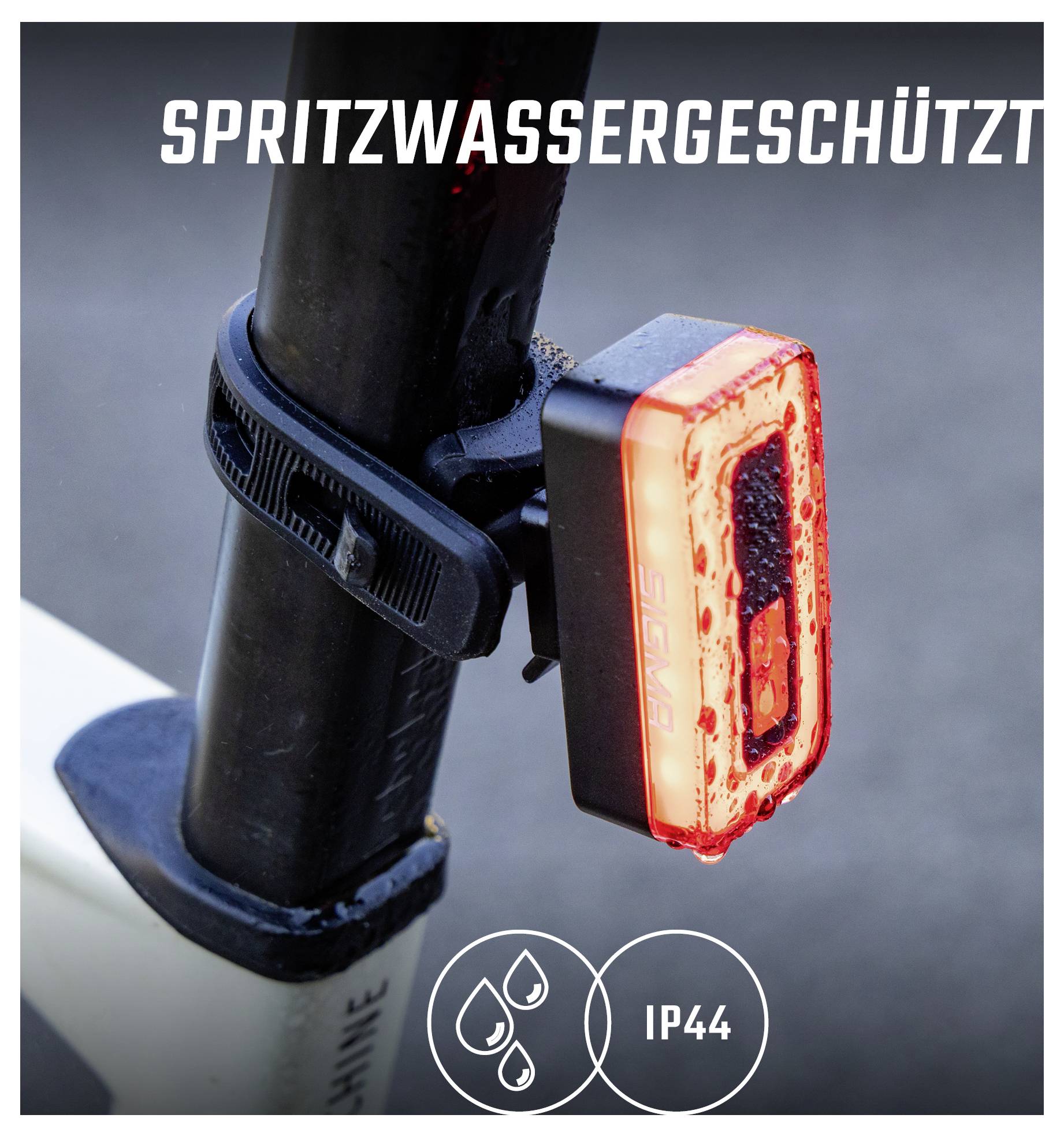 Nahaufnahme eines am Rahmen montierten roten Fahrradrücklichts mit Aufdruck 'SPRITZWASSERGESCHÜTZT' und Kennzeichnung 'IP44'.