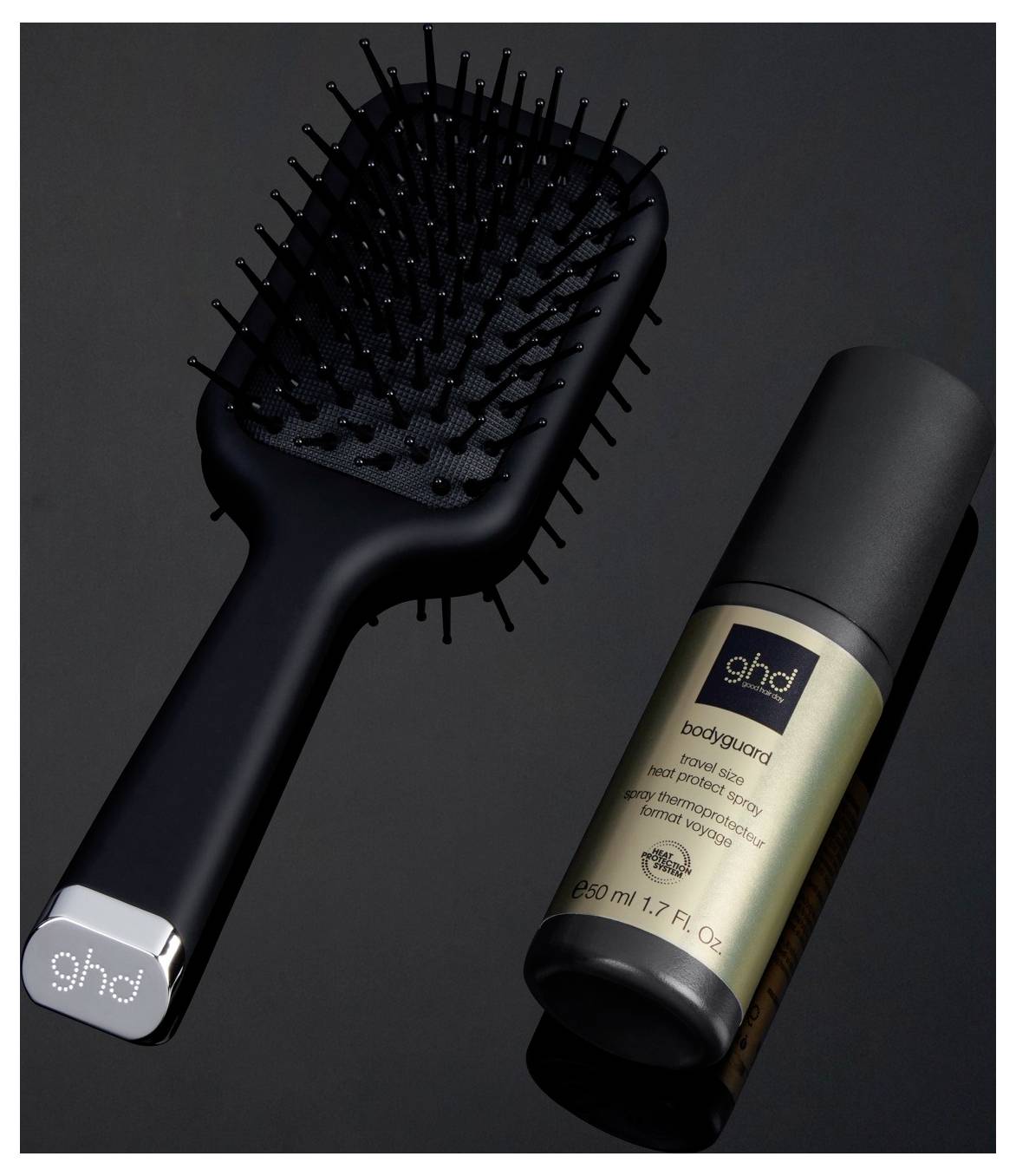 Schwarze ghd Haarbürste und passende Bodyguard Styling Spray Flasche auf dunklem Hintergrund.