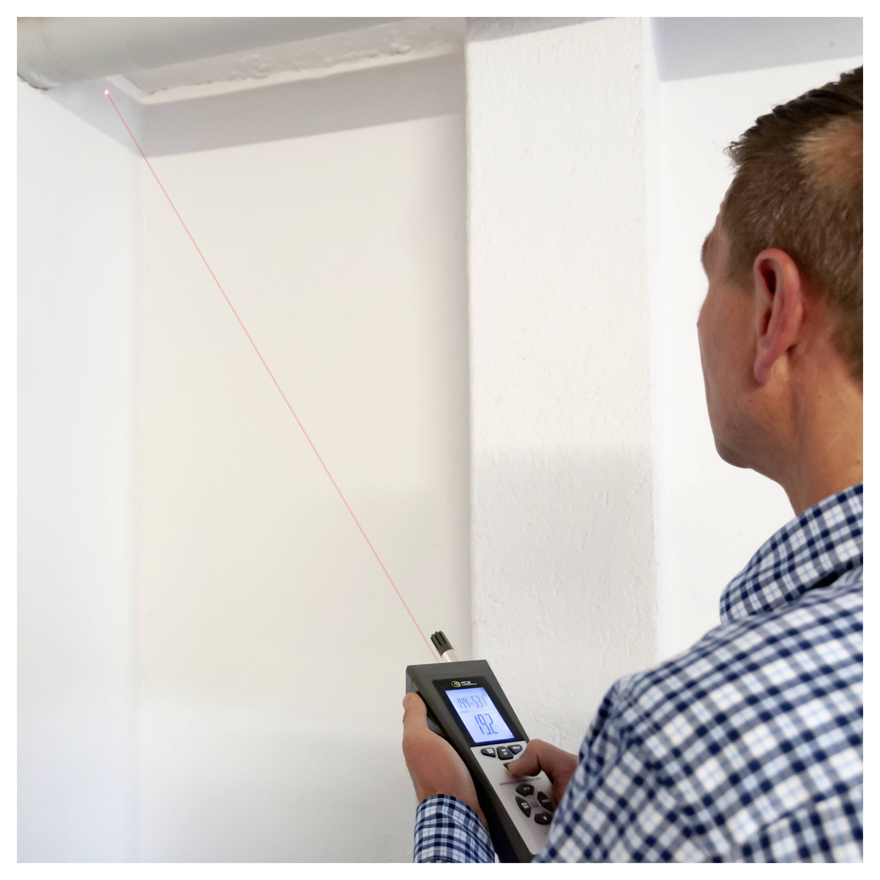Ein Arbeiter nutzt ein Laser-Entfernungsmessgerät, um eine Wandecke in einem weißen Raum zu messen.