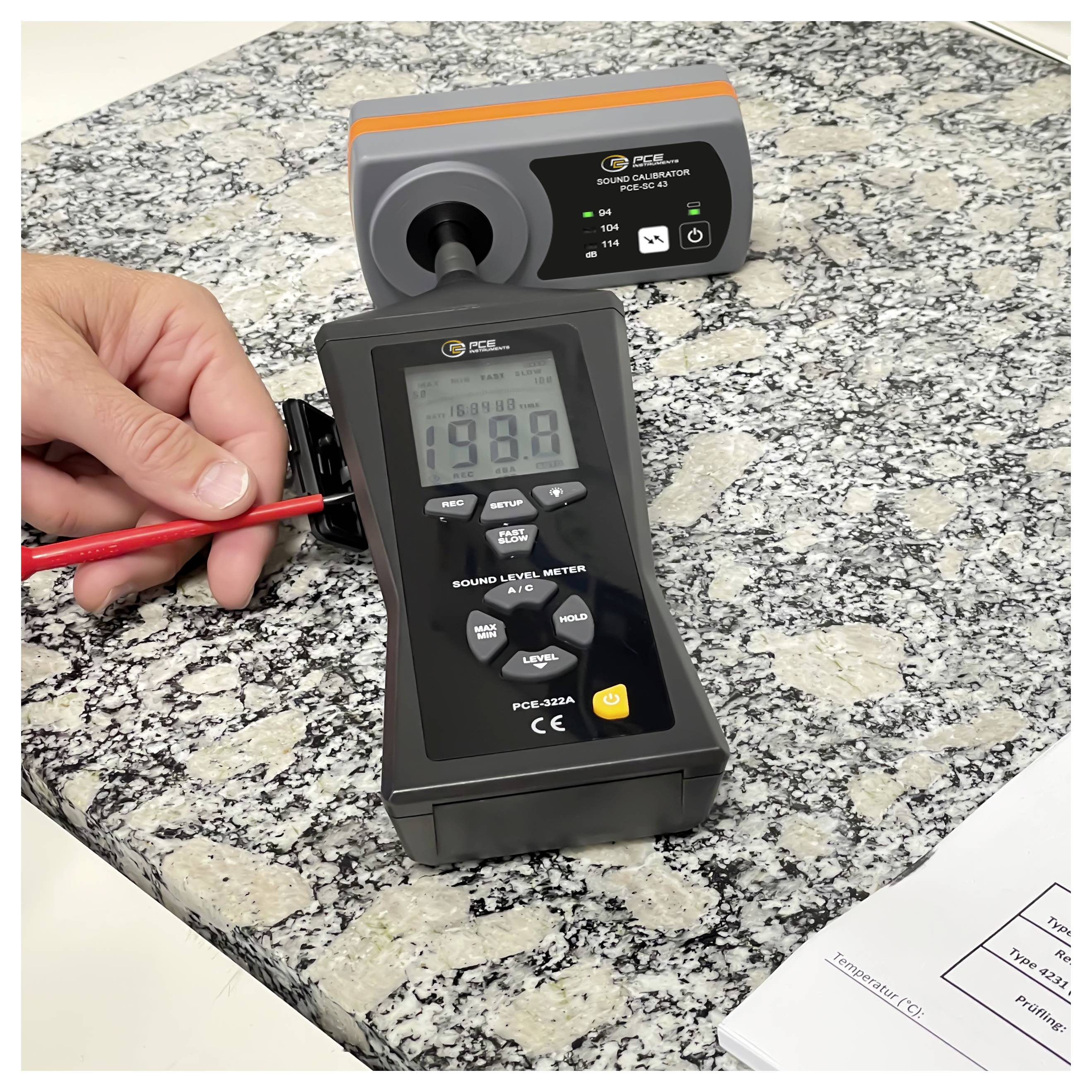 Hand hält eine Sonde eines Schallpegelmessers gegen eine Granitarbeitsplatte, während ein digitales Dezibel-Messgerät die Messung anzeigt.