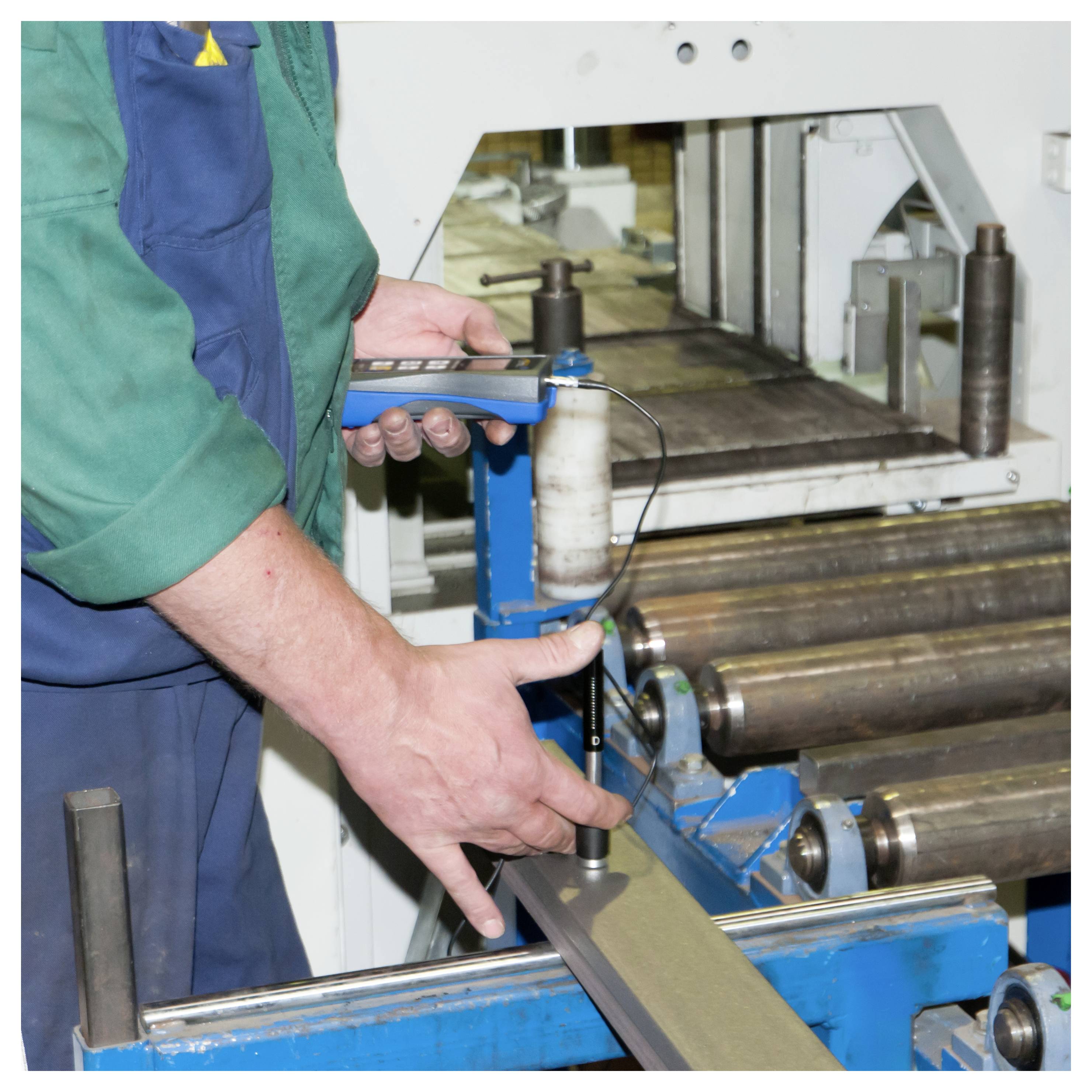Arbeiter, der ein tragbares Messinstrument verwendet, um einen Metallstreifen auf einer industriellen Walzmaschine zu messen.