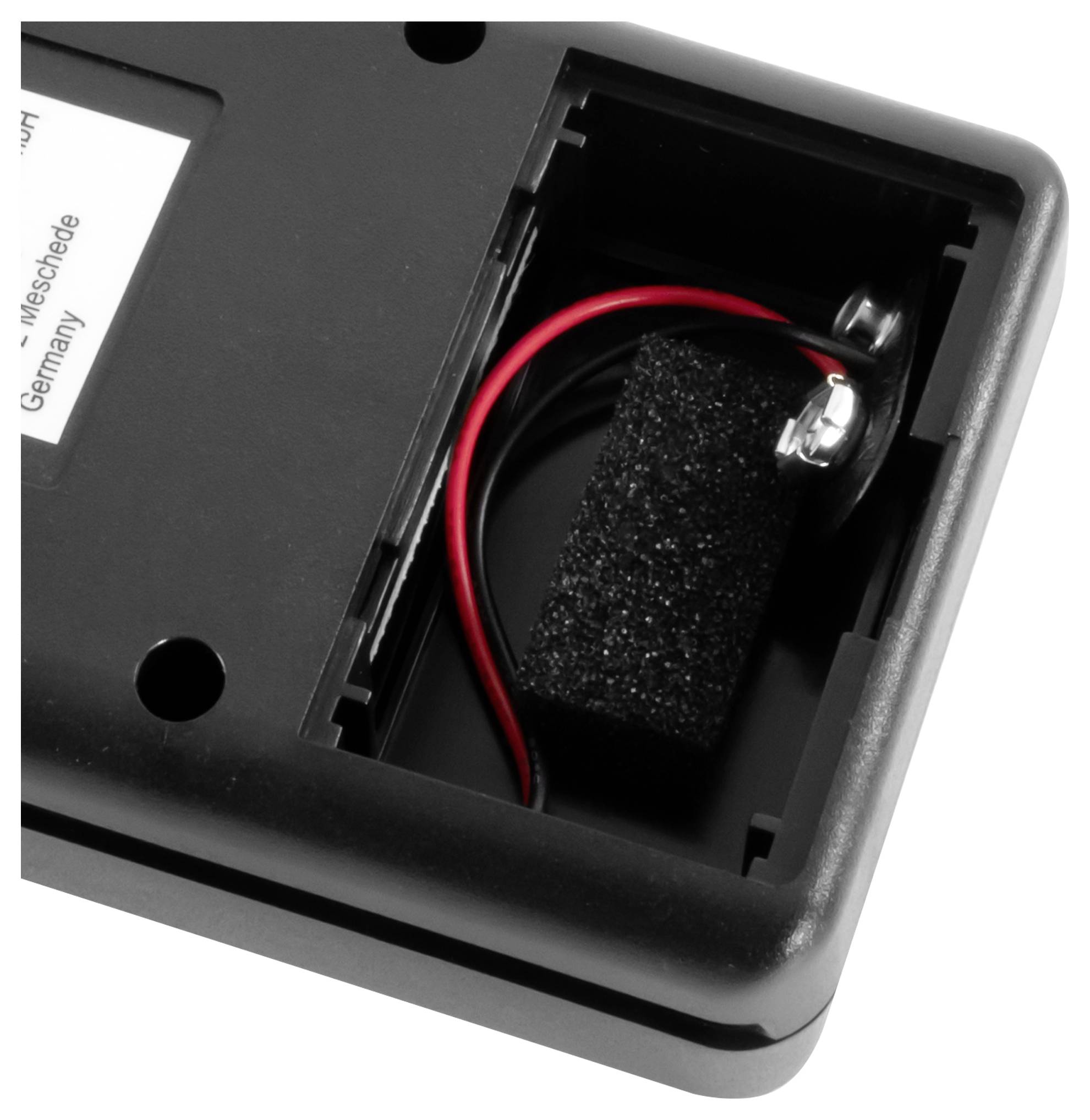 Nahaufnahme eines schwarzen Kunststoffgerätekompartiments mit einem roten Draht, der mit einer Batterie oder einer Stromklemme in einem offenen Gehäuse verbunden ist.
