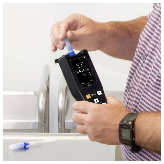 Person, die ein tragbares blaues Testgerät verwendet, um die Wasserqualität zu messen, und eine Probenröhre in einem Waschbereich einfügt.