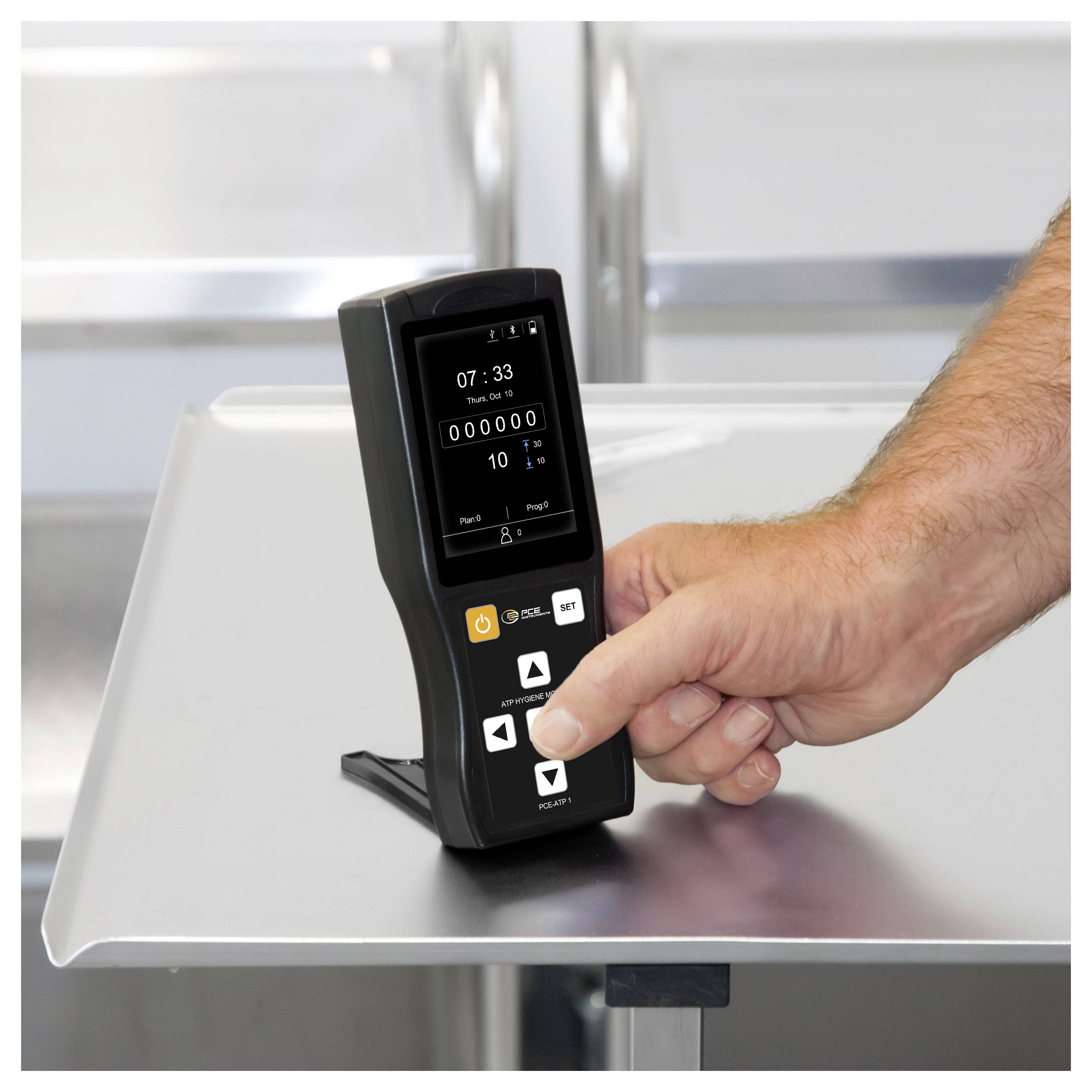 Hand drückt Tasten auf einem schwarzen digitalen Steuergerät mit einem kleinen Display, das 07:33 und Zähler 000000 auf einem Metalltisch anzeigt.