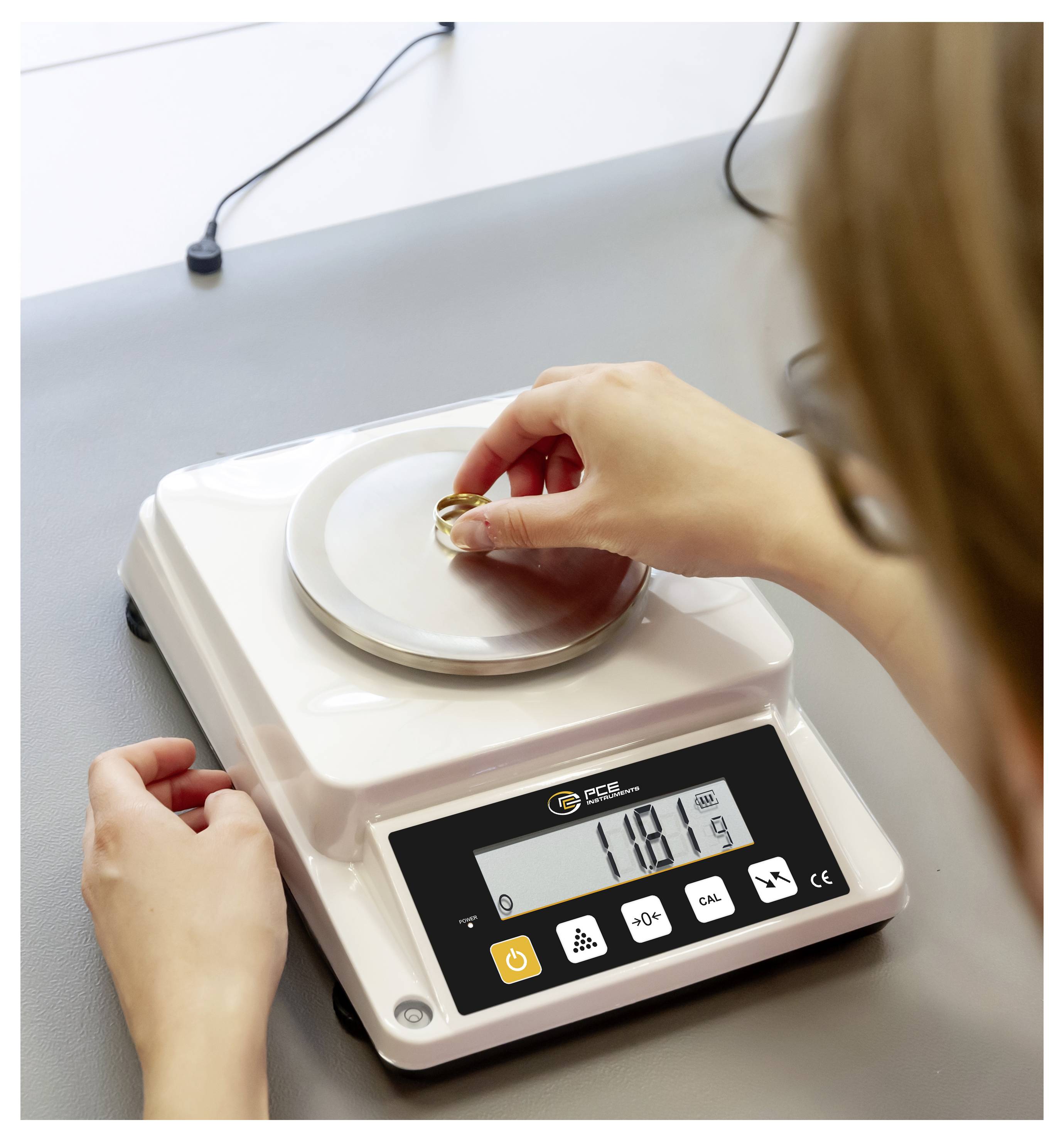 Eine Person wiegt einen Ring auf einer digitalen Juwelier-Waage, die 11,8 g anzeigt.