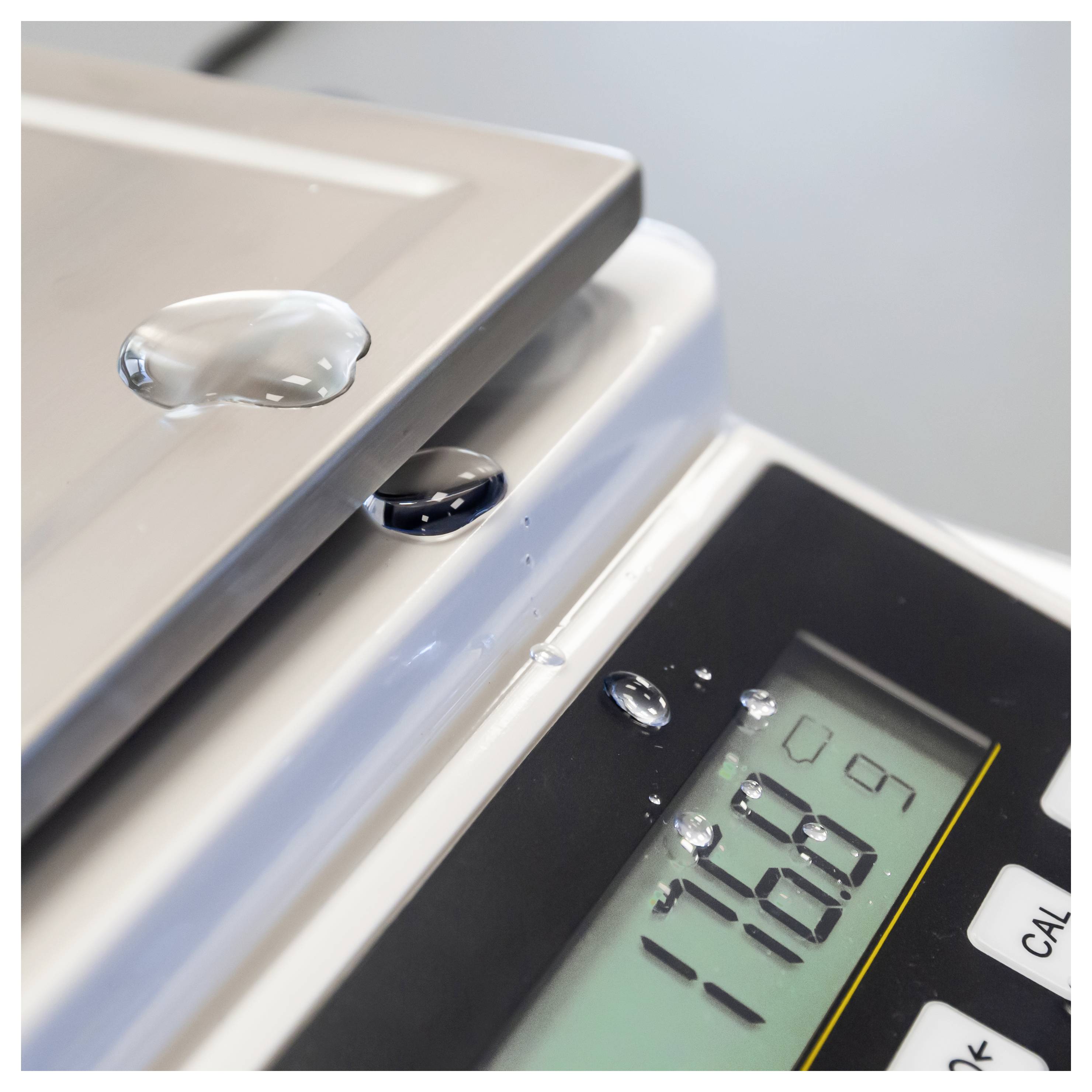 Wassertropfen auf einer digitalen Waage neben einem geschlossenen silbernen Gerät, wobei das Display -18,9 anzeigt
