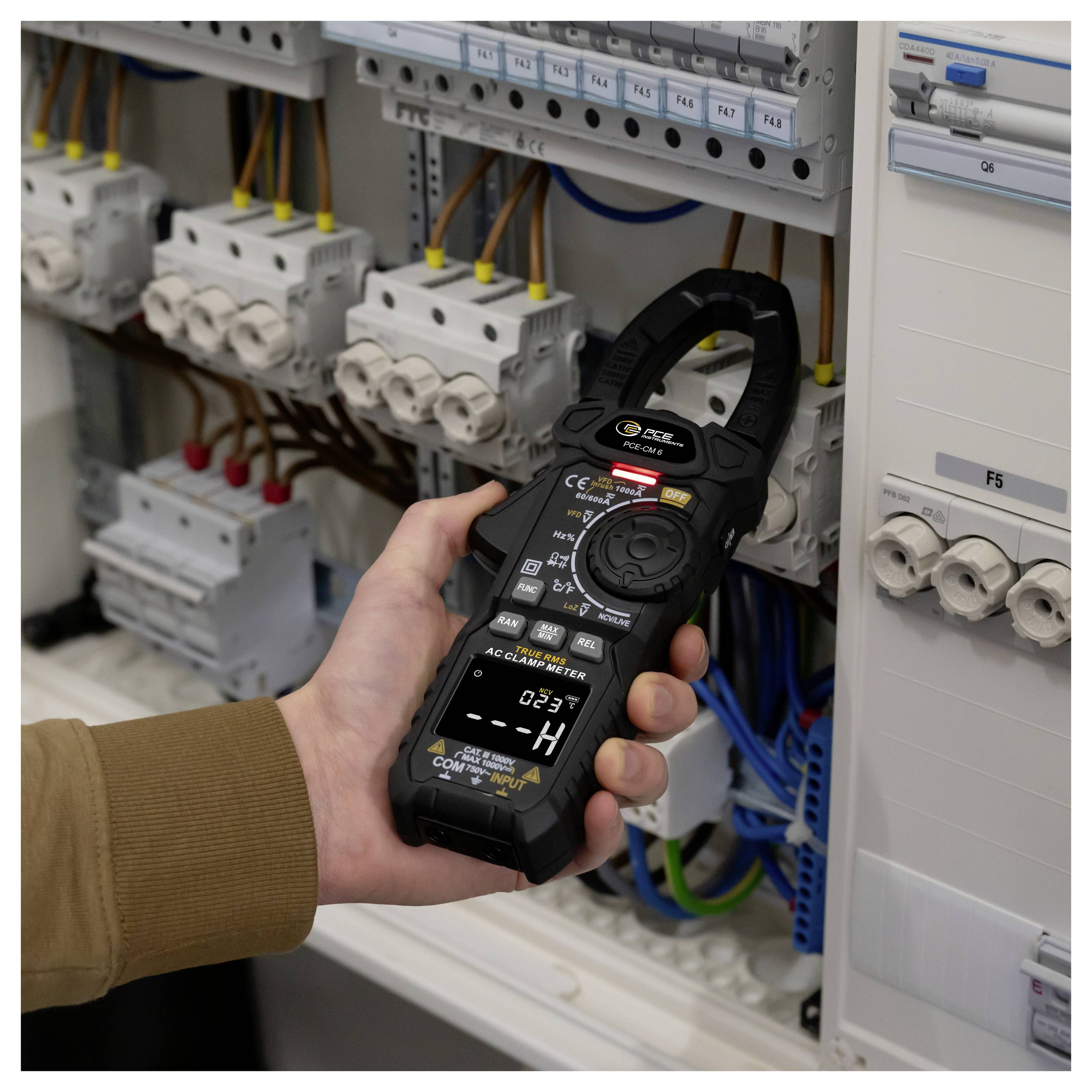 Hand hält ein Stromzangenmessgerät in einem elektrischen Schaltschrank und misst die Stromstärke auf Verdrahtung und Leistungsschaltern.