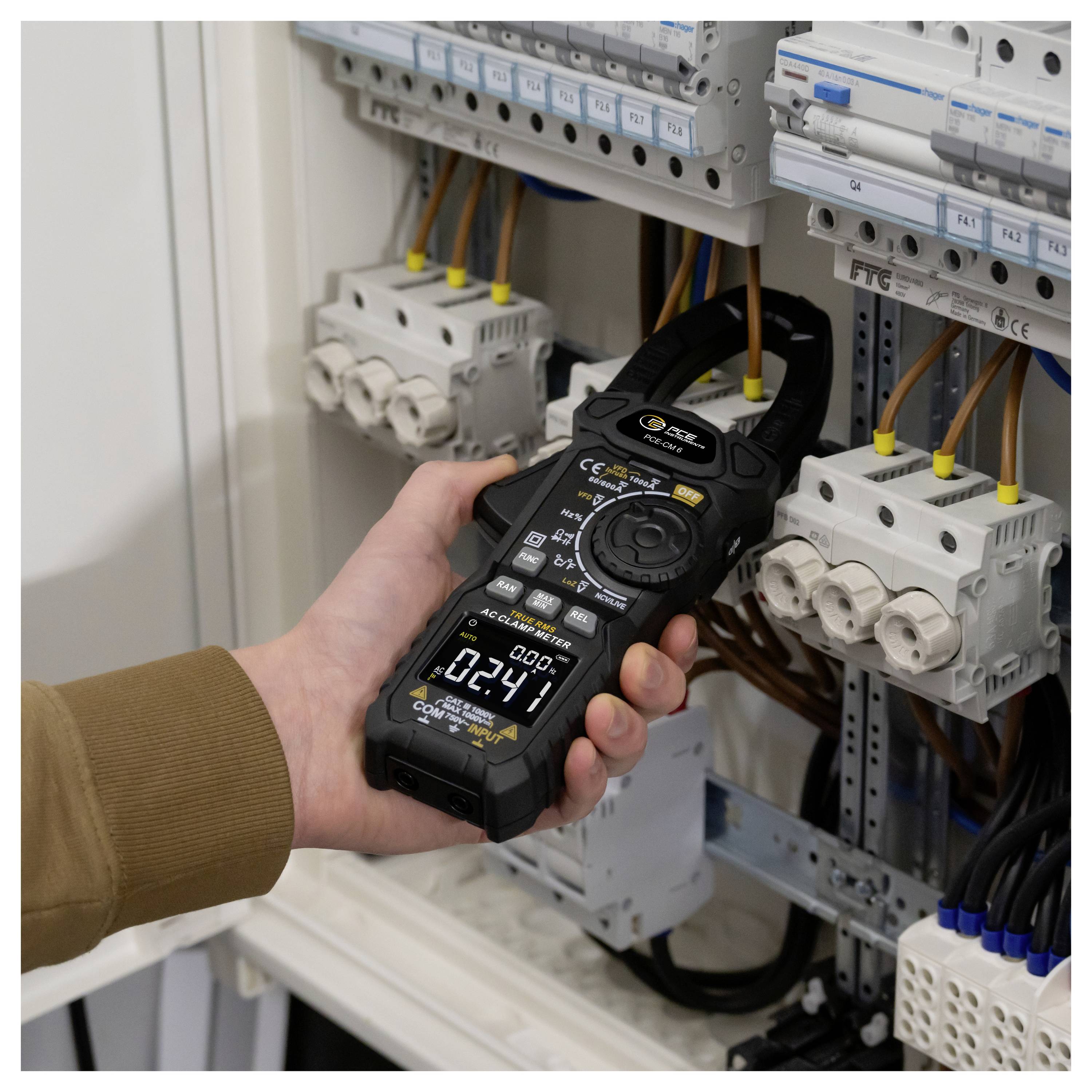 Tragbares elektrisches Zangenamperemeter, das die Verkabelung in einem offenen Elektrosteuerungsfeld mit Leistungsschaltern und angeschlossenen Kabeln prüft.