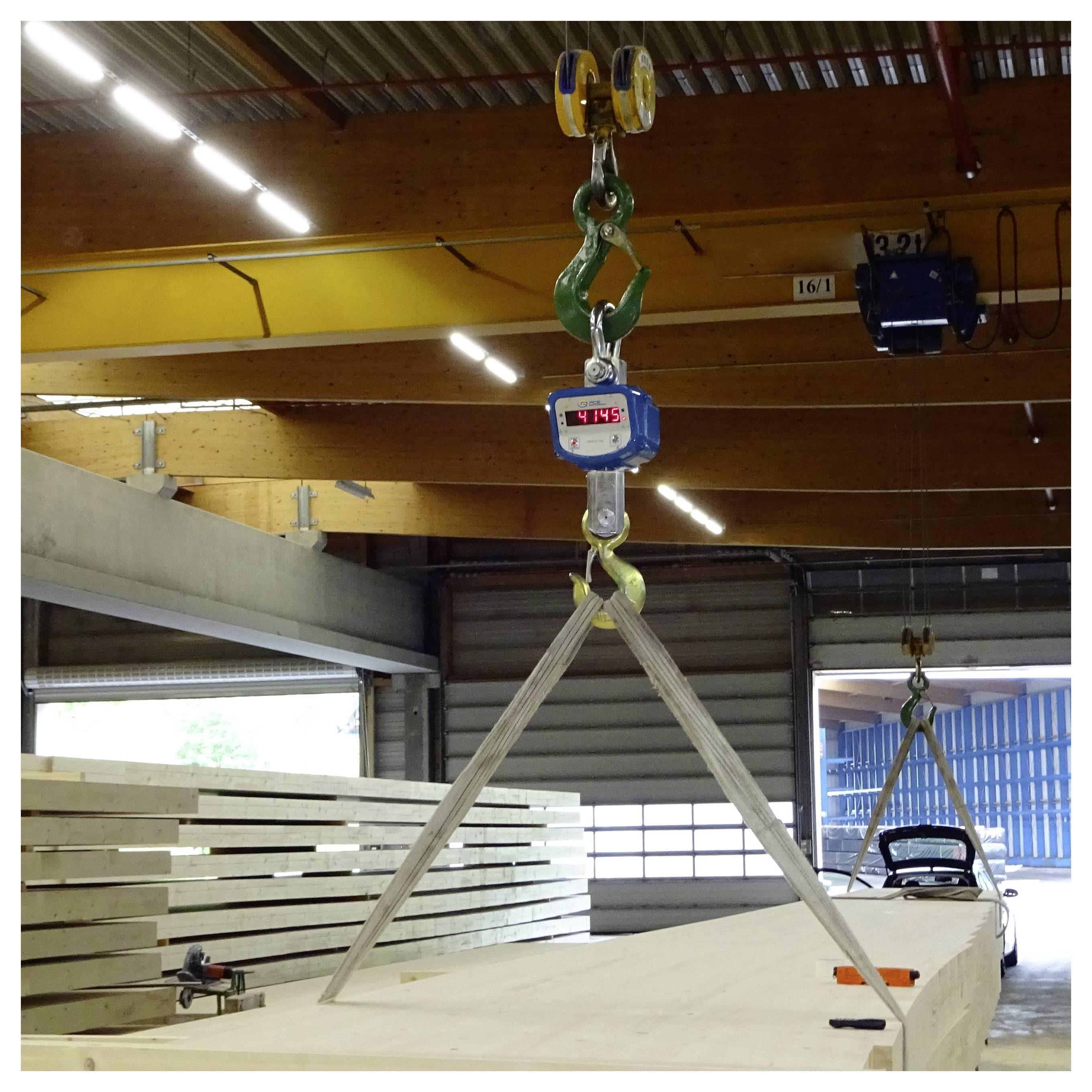 Laufkran hebt einen großen Holzbalken mit Schlingen in einer Werkstatt an, das Gewicht wird auf einer hängenden digitalen Waage angezeigt.