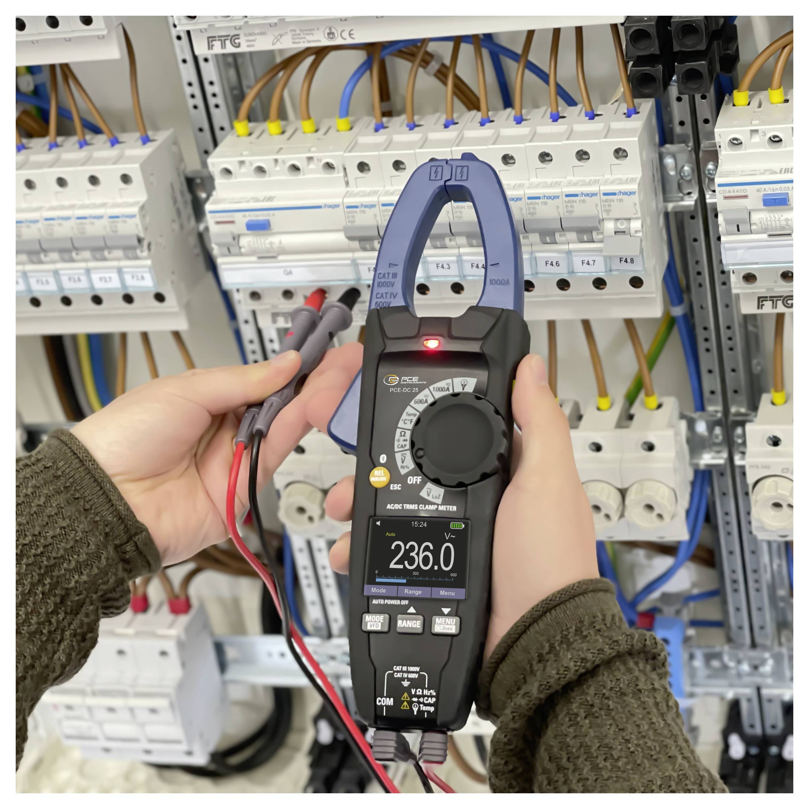 Person, die ein Elektroschaltfeld mit einem Stromzangenmessgerät testet, das 236,0 Volt anzeigt, umgeben von Leitungsschutzschaltern und Verkabelung.