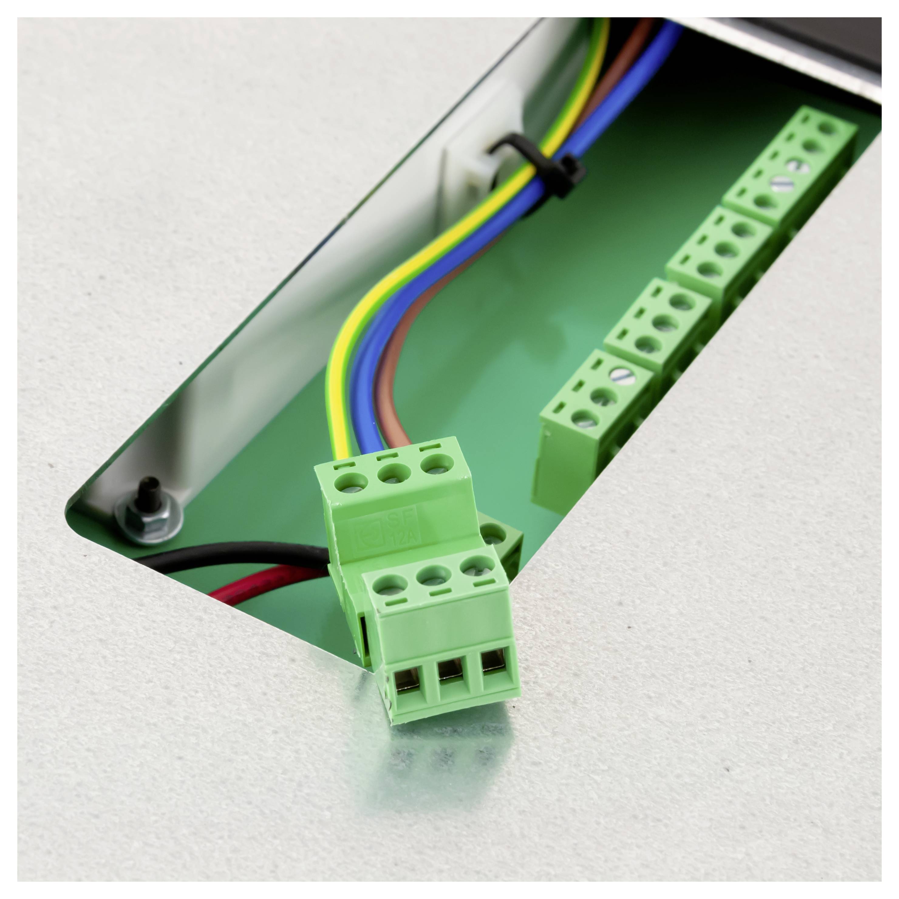 Nahaufnahme von grünen elektrischen Klemmenblöcken und mehrfarbigen Drähten in einem Metallpanelausschnitt.