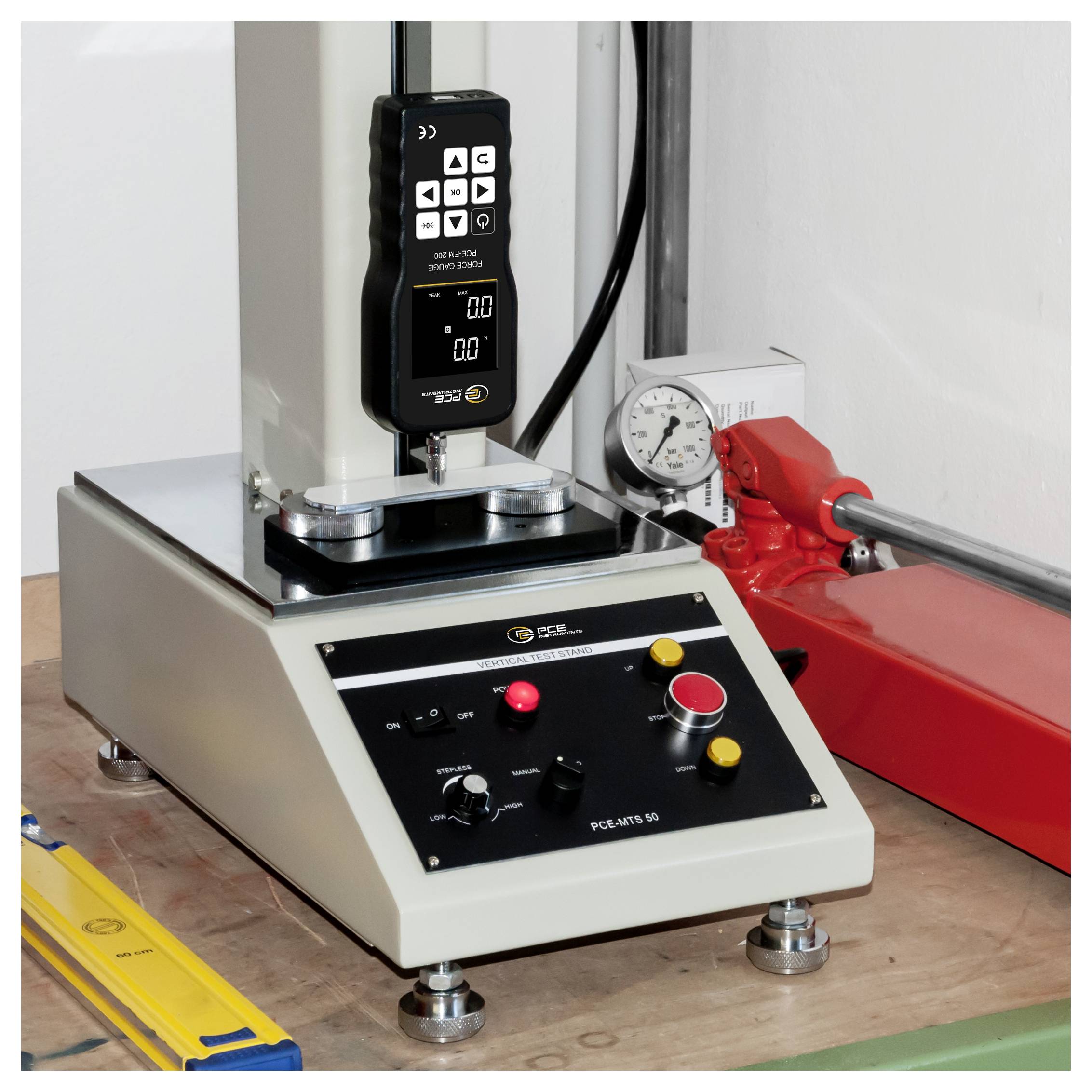 Materialprüfmaschine im Labor mit digitaler Bedienplatte, Druckmessgerät und rotem Spannarm auf einer Werkbank.