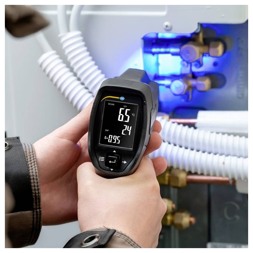 Eine Person hält ein digitales Infrarot-Thermometer, das 6,5°C anzeigt, gegen leuchtend blaue HVAC- oder Rohrleitungs- und Ventilrohre.