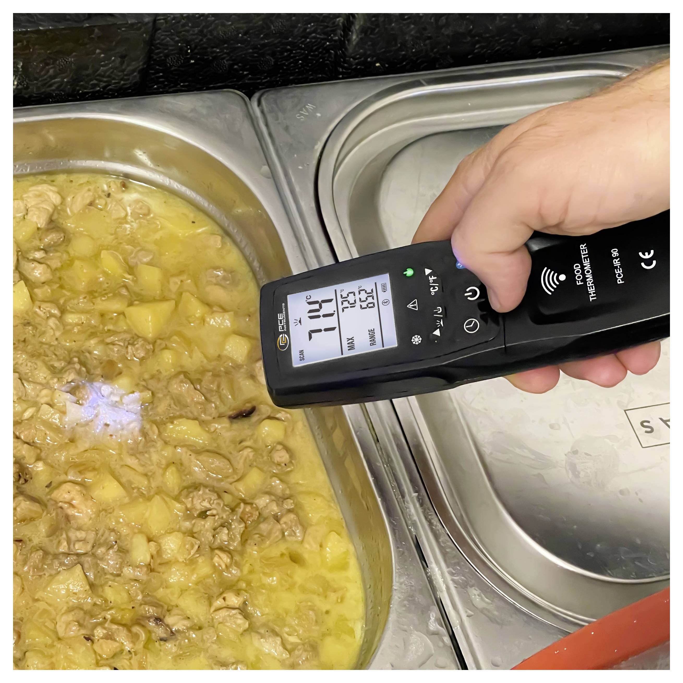 Hand, die ein digitales Fleischthermometer über ein Tablett mit gekochtem Fleisch und Kartoffeln in Soße hält und eine Temperaturanzeige von 71,4°C zeigt.