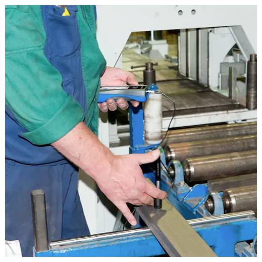 Arbeiter, der eine Metallschneid- oder Schleifmaschine bedient und einen langen Streifen durch Walzen in einer Werkstatt führt.