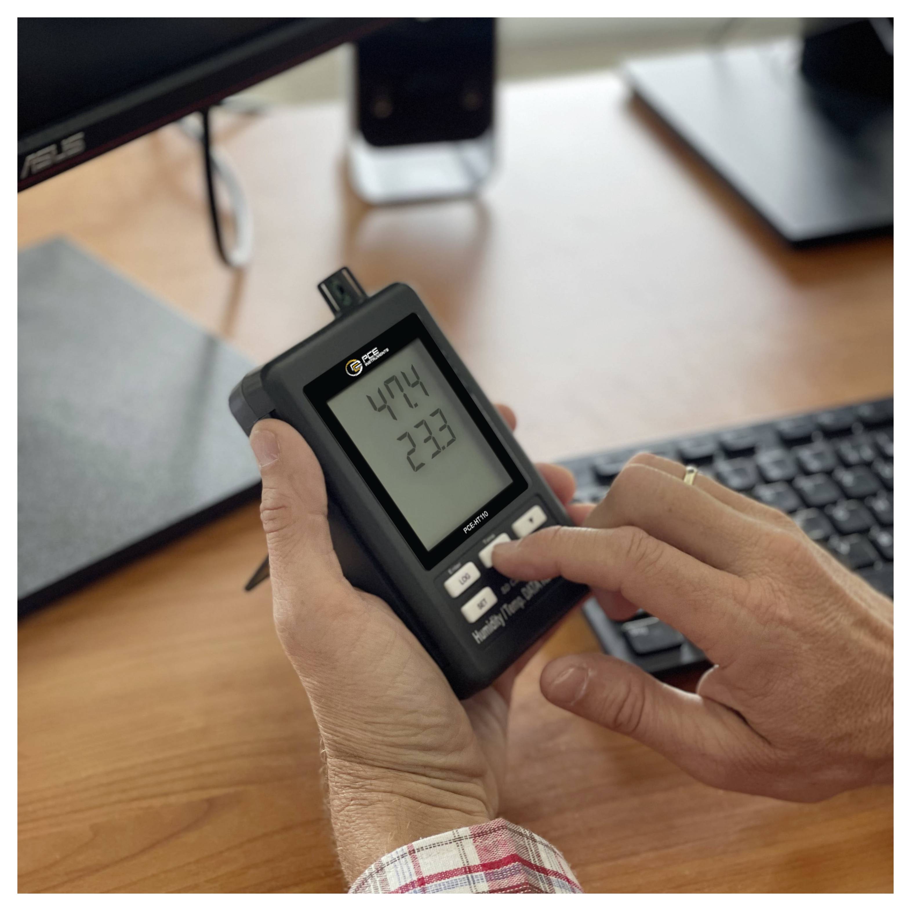 Eine Person, die ein tragbares digitales Strommessgerät verwendet, mit einem Finger, der einen Knopf drückt; der Bildschirm zeigt Messwerte von 47,4 und 2,37 auf einem Schreibtisch an.