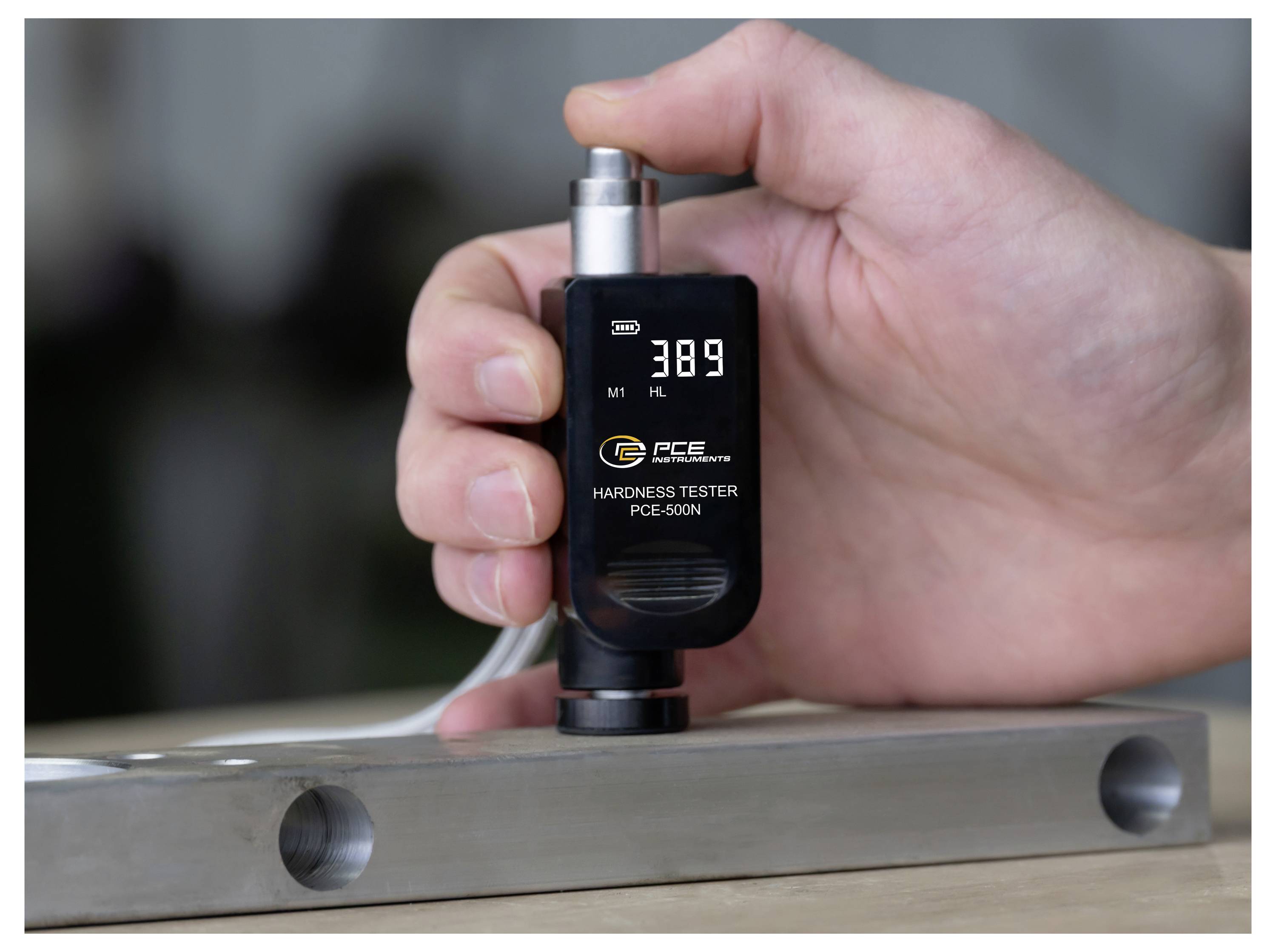 Tragbarer digitaler Härtetester, der einen Metallblock misst und einen Messwert von 389 auf dem Display anzeigt.