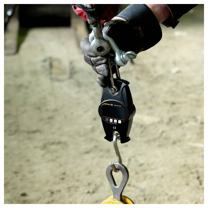 Handschuhgetragener Arbeiter befestigt ein schwarzes Sicherheitsschutzvorrichtungsgerät an einem Metallhaken an einem Seil oder Kabel in einer Baustelle.