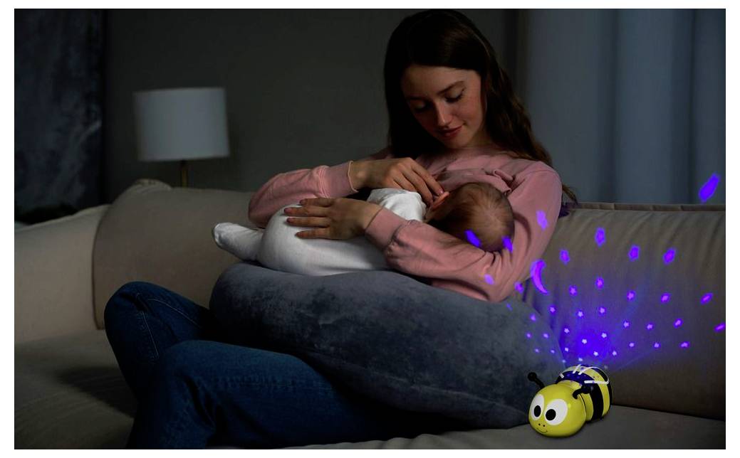 Eine Mutter stillt ihr Baby auf einem Sofa, während eine Spielzeugbiene blaue Lichter durch das Zimmer projiziert.
