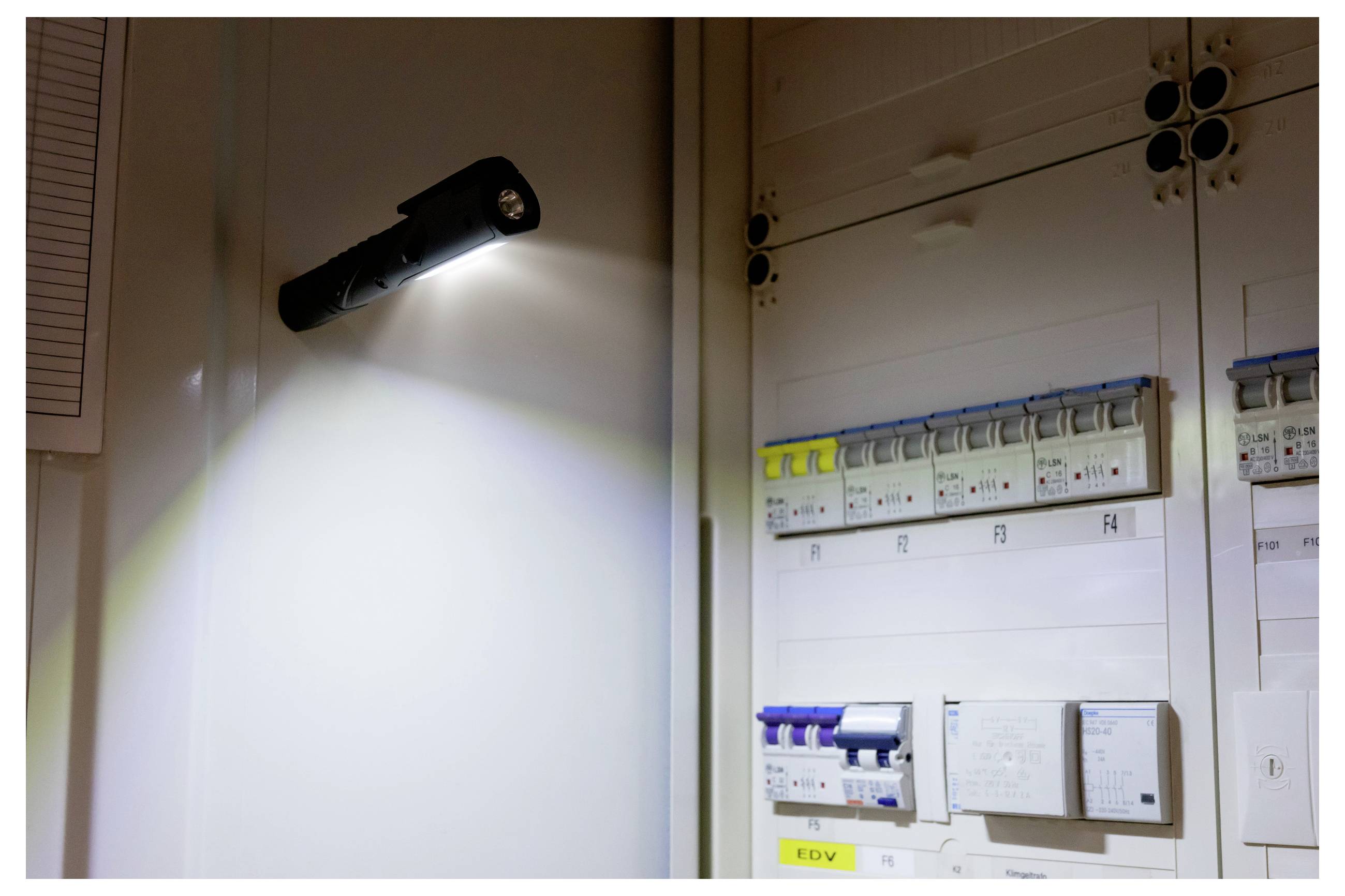 An der Wand montierte LED-Leuchte, die über ein elektrisches Schaltfeld mit beschrifteten Schaltern und Steuermodulen scheint