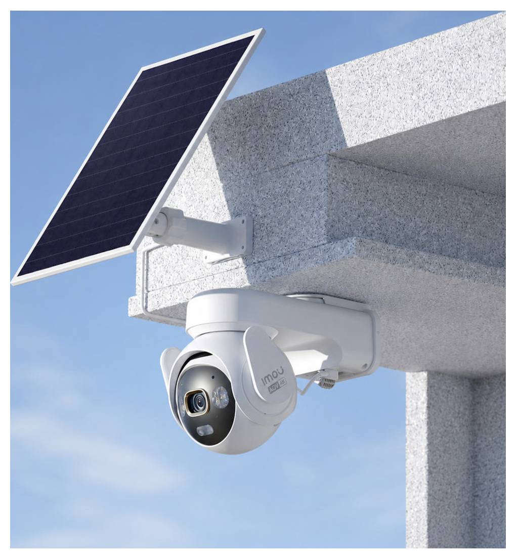 Solarbetriebene Überwachungskamera an einer Gebäudeecke unter einem kleinen Solarpanel vor blauem Himmel montiert.