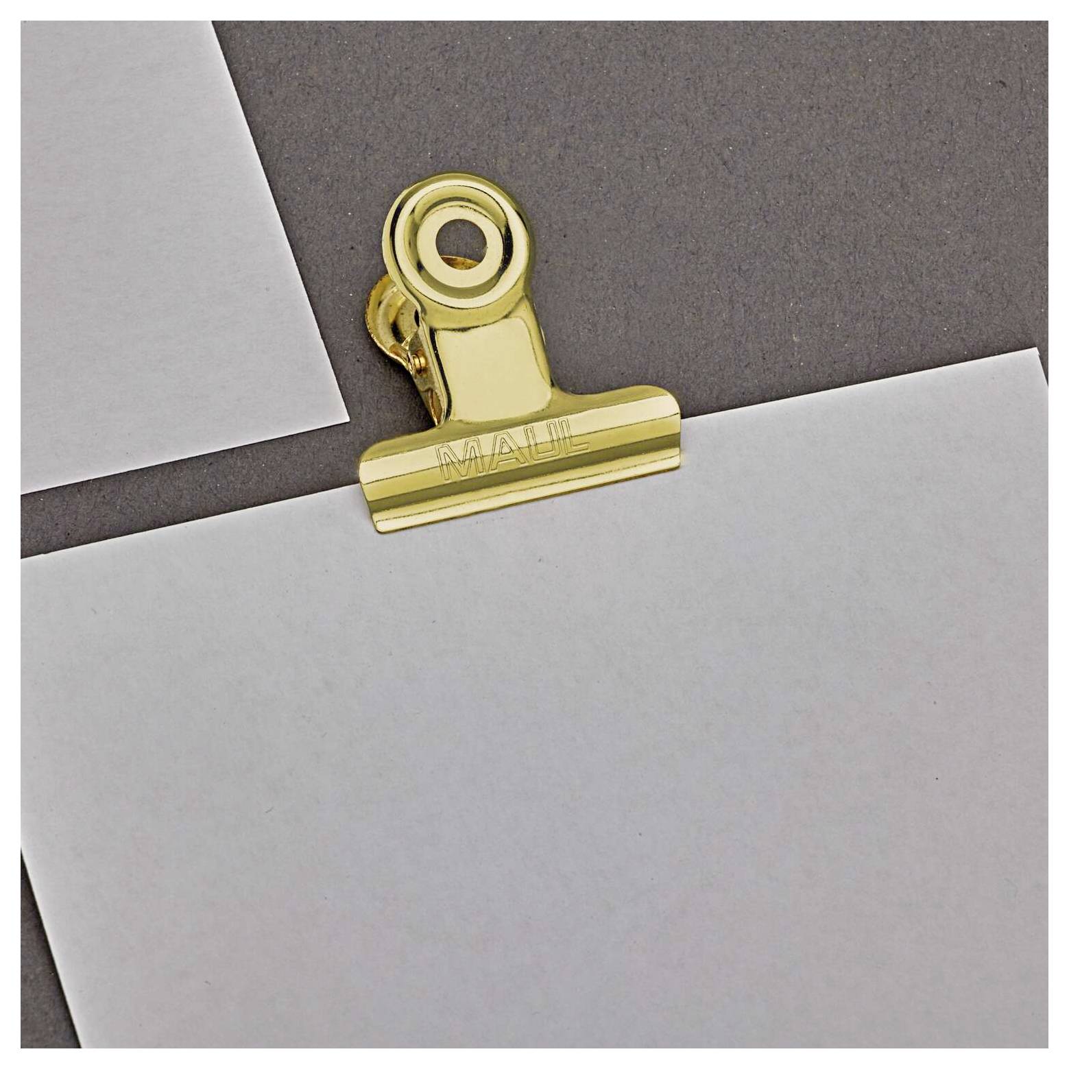 Goldfarbene Briefklammer, die mehrere graue Blätter Papier auf einer dunklen Oberfläche zusammenhält.