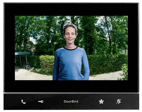 DoorBird Video-Türsprechanlage zeigt eine Frau, die draußen vor Bäumen und einem Weg steht.