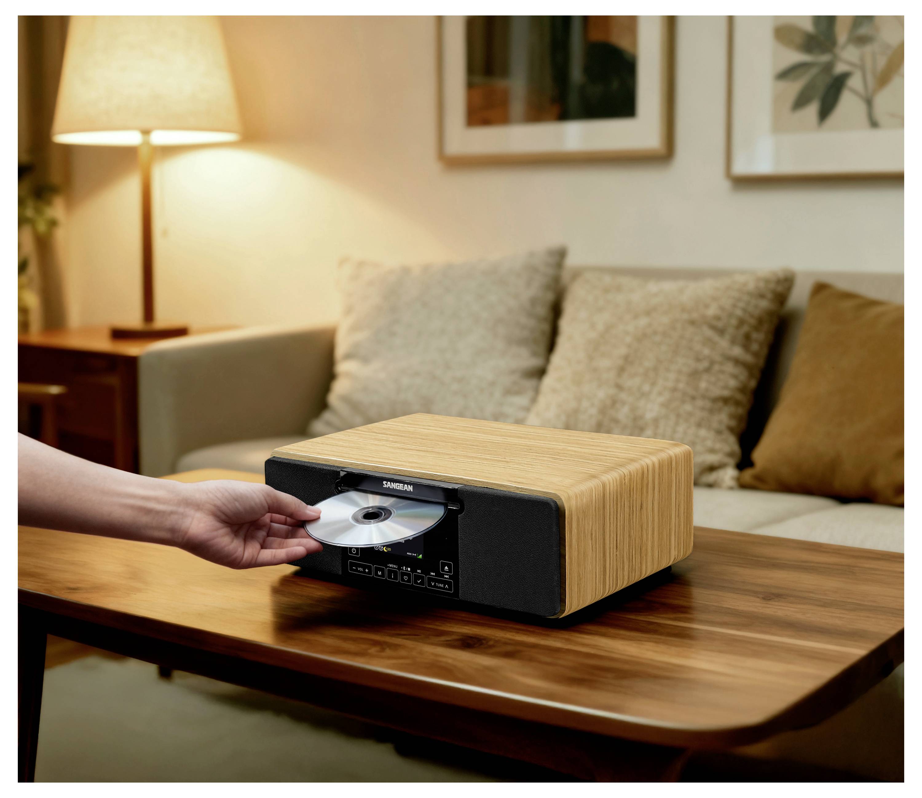 Eine Hand führt eine CD in ein kompaktes Stereosystem mit Holzmaserung auf einem Couchtisch in einem gemütlichen Wohnzimmer ein.