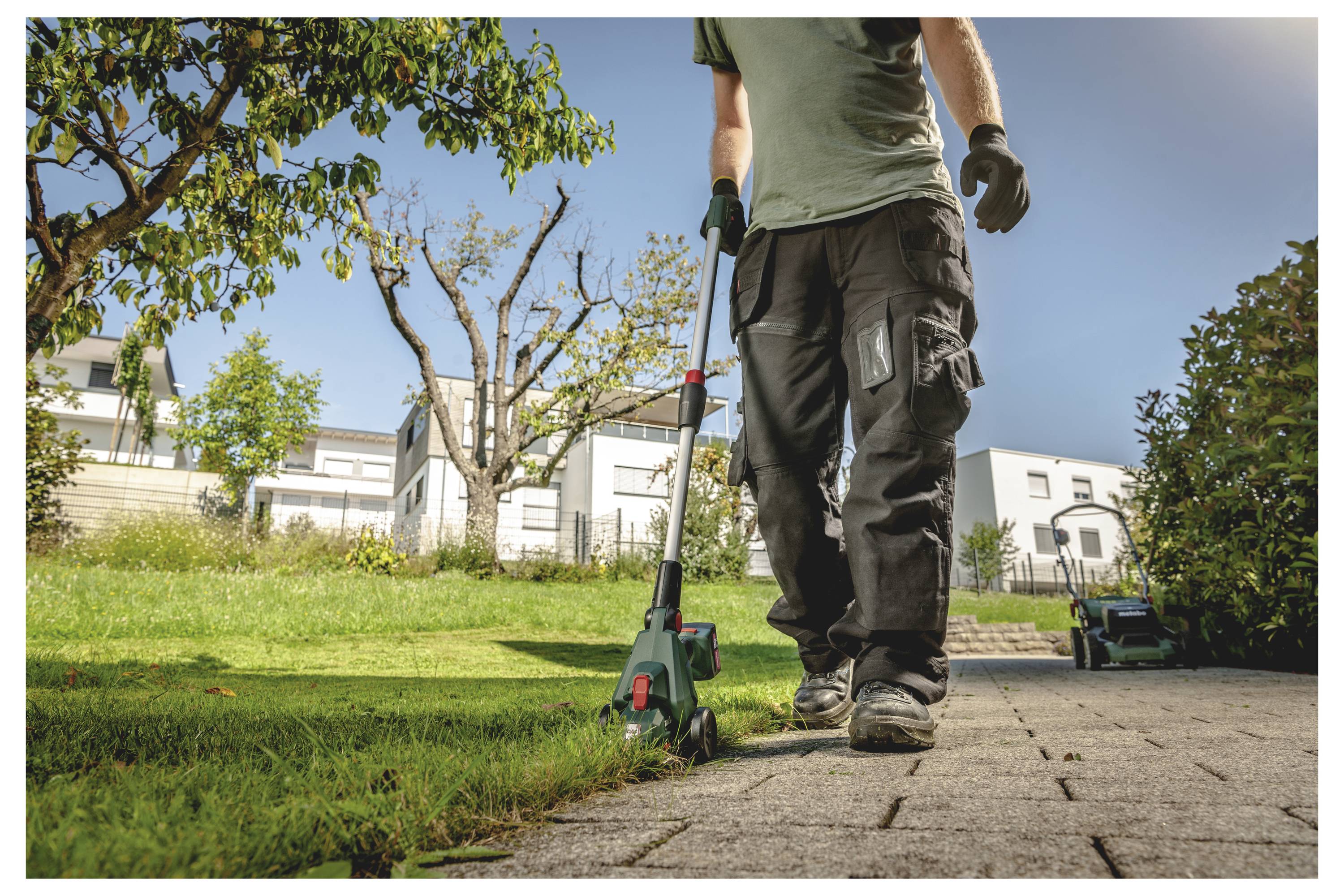 Ein Arbeiter steht auf einem Gartenweg mit einem Fadentrimmer und schneidet Gras neben einem Rasen in einem Vorstadtgarten.