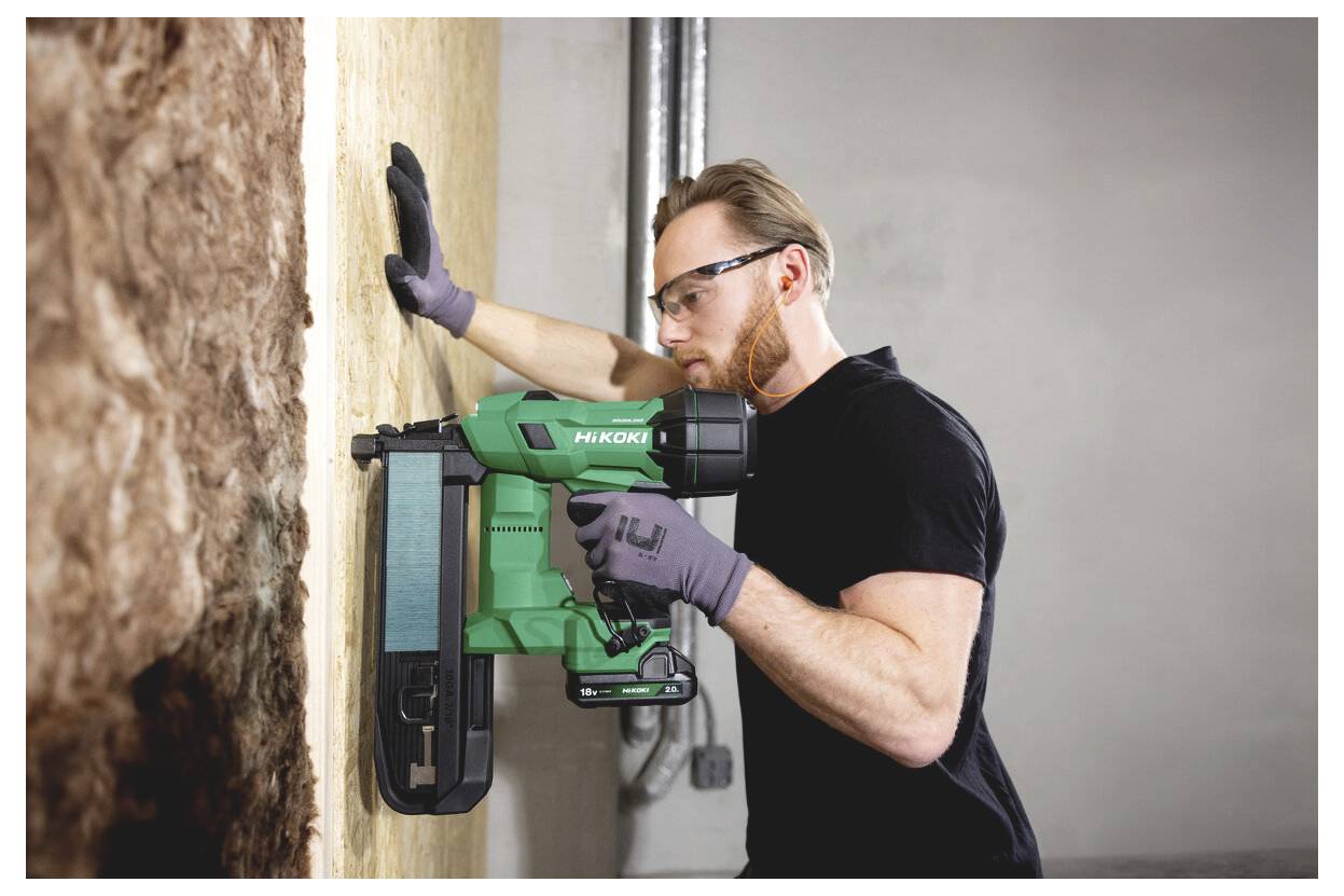 Ein Arbeiter verwendet eine grüne Hikoki-Nagelmaschine, um Isolierplatten an einer Wand auf einer Baustelle zu befestigen.
