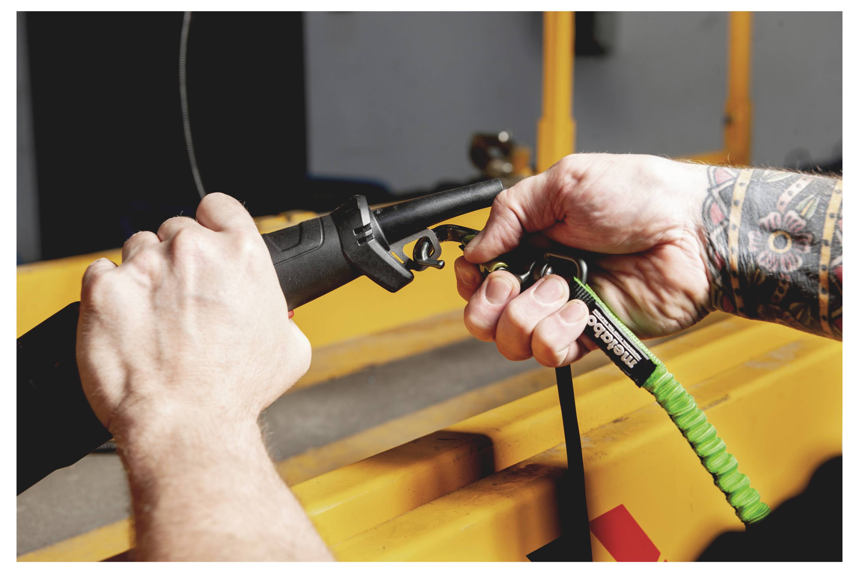 Zwei Hände verbinden ein schwarzes Kabel mit grüner Spulenentlastung mit gelbem Industrieequipment, wahrscheinlich um einen Strom- oder Steuerstecker zu befestigen.
