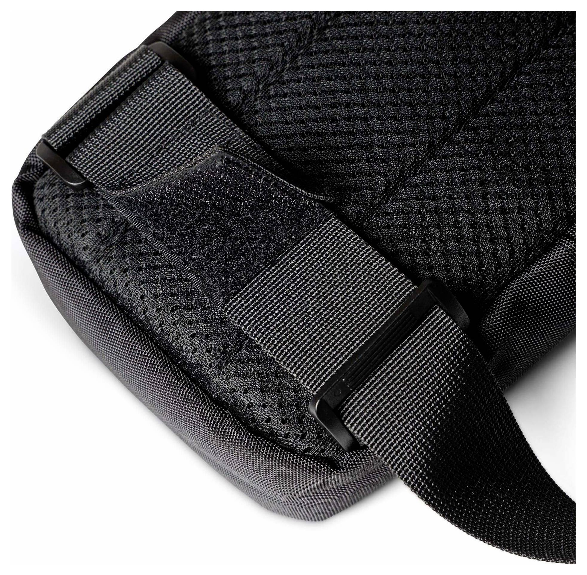 Nahaufnahme einer schwarzen gepolsterten Taschenecke mit verstellbarem Webbandriemen und Kunststoffschnalle auf strukturiertem Stoff.